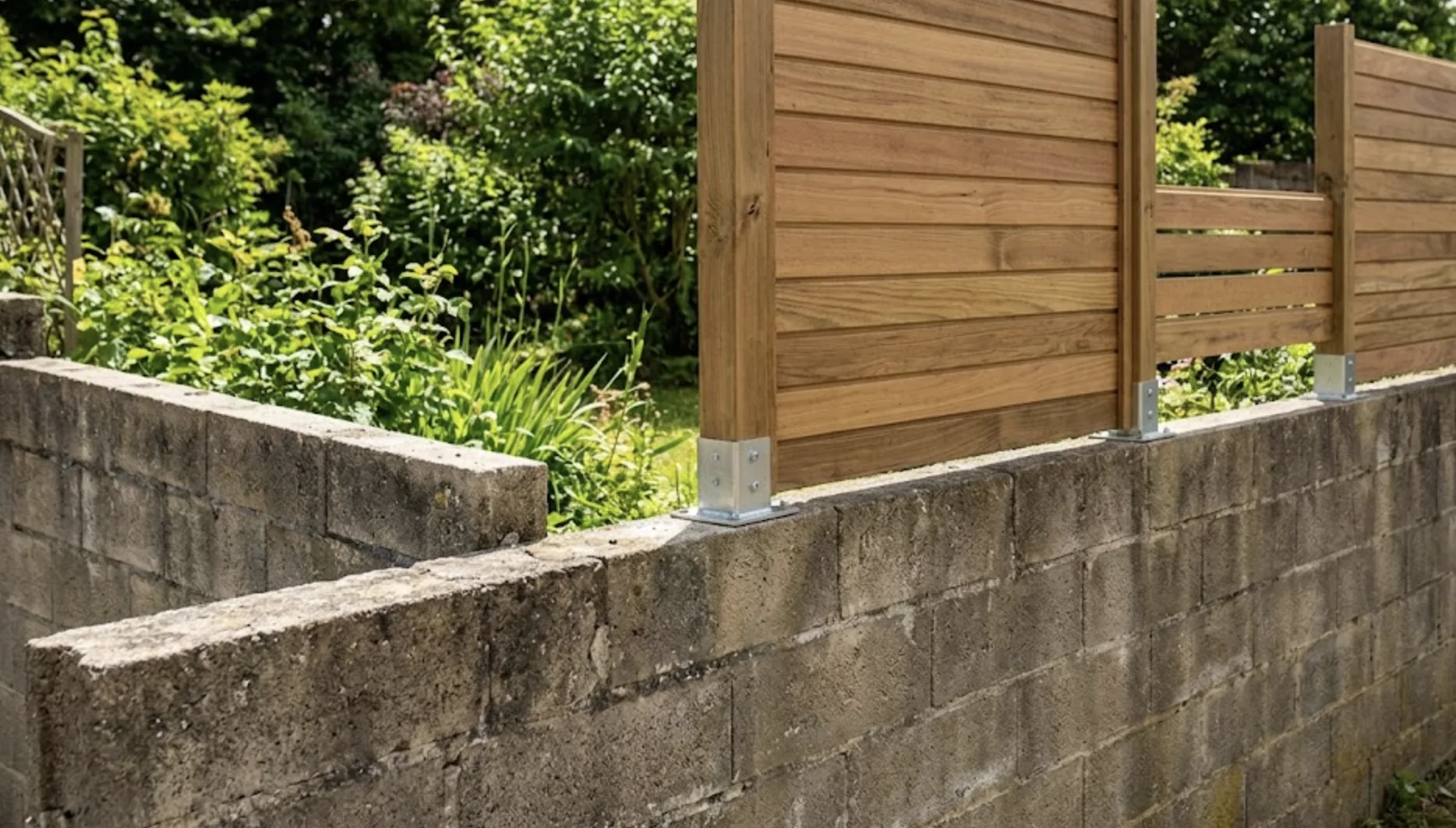 Muret en parpaing brut sur lequel a été fixée une extension en panneaux de bois claustra sur platines métalliques, jardin verdoyant en arrière-plan